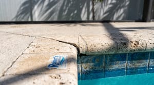 Cracked waterline tile and stone coping on a sun-baked Miami pool deck